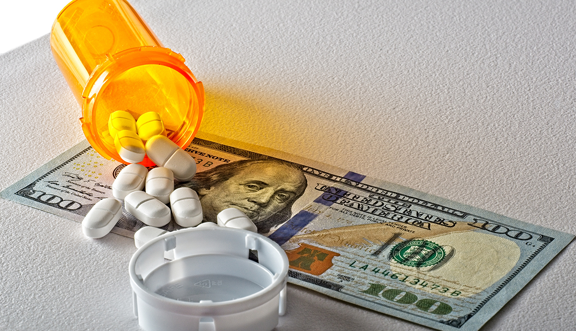 a bottle of white pills are spilled across a one hundred dollar bill