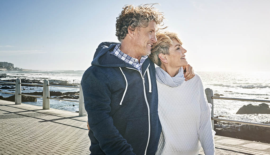 a mand an a woman walking arm in arm on a boardwalk next to the ocean