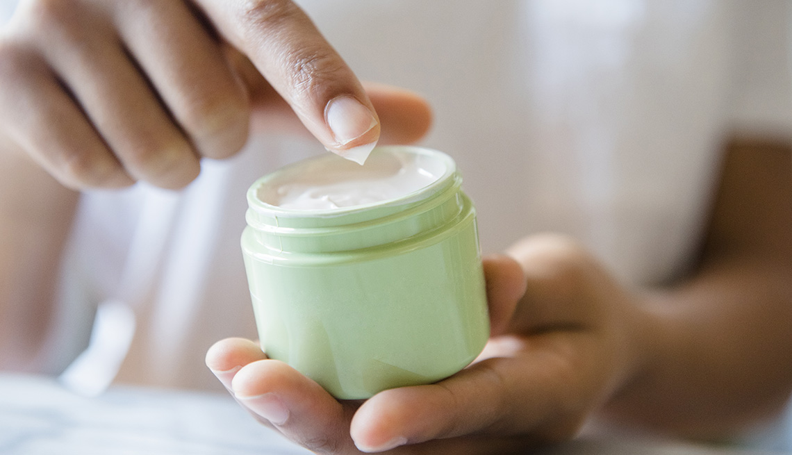 A closeup of a woman dipping her finger in jar of moisturizer