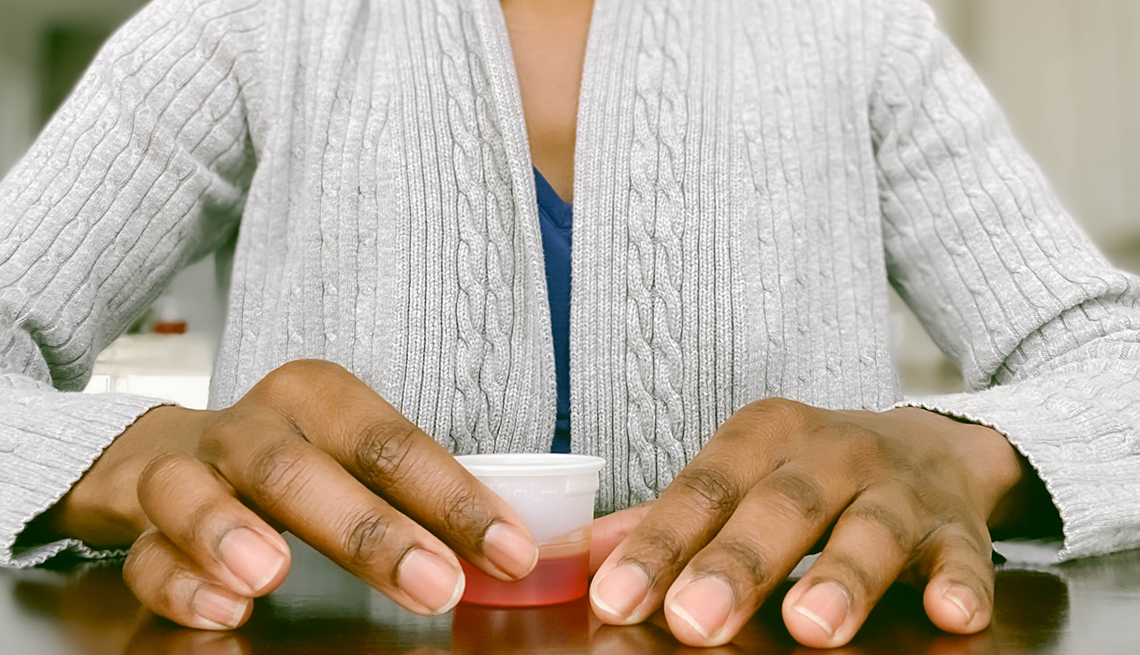 close up of a woman's hands holding a small cup of cough syrup
