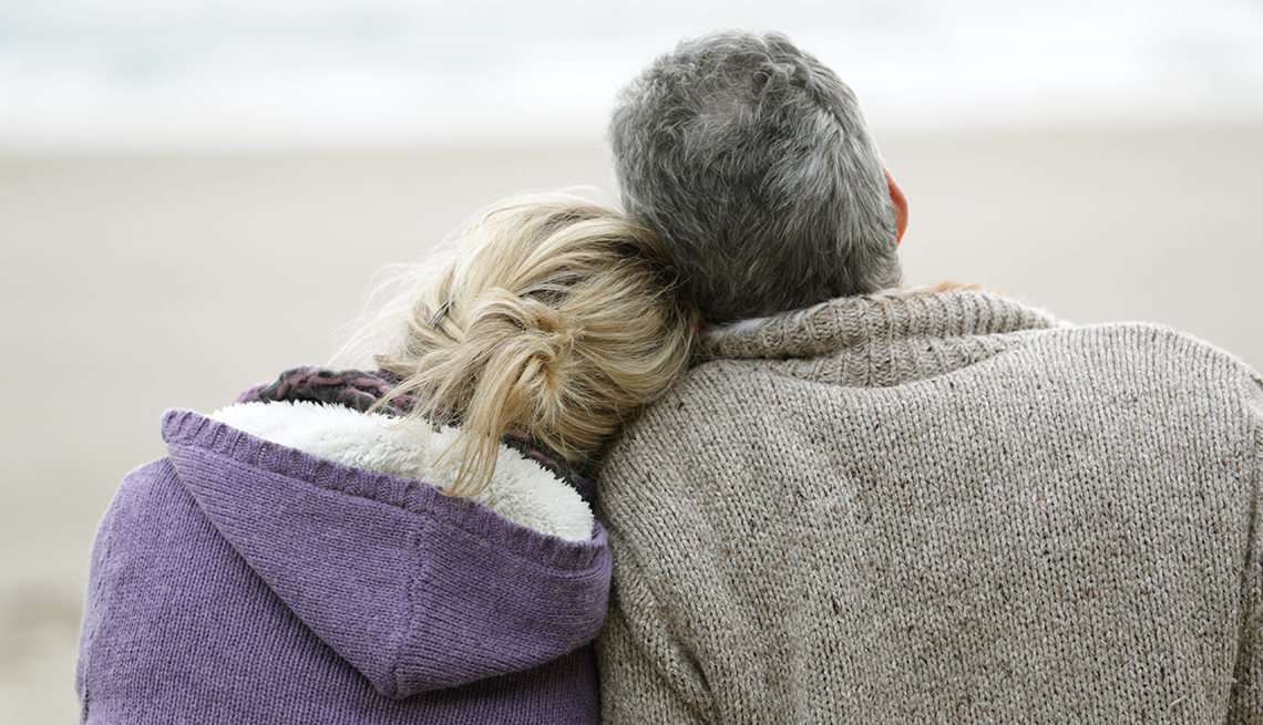 man and woman cuddling on the beach, looking at the ocean