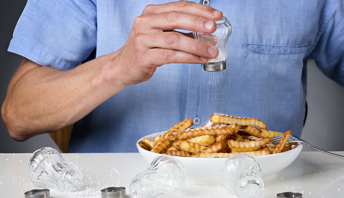 A person is pouring salt onto french fries