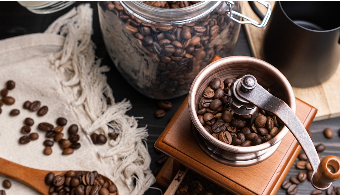 Roasted coffee beans in a glass jar and a coffee grinder
