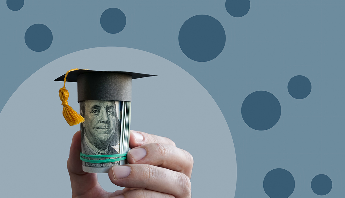 Fingers hold a roll of cash with Ben Franklin's face facing camera; there's a graduation cap with tassel on top of the cash roll. 