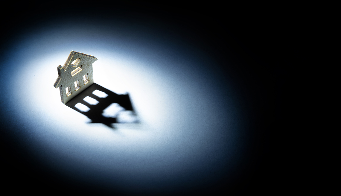 Silueta de una casa hecha en madera iluminada y con su sombra proyectada en el suelo