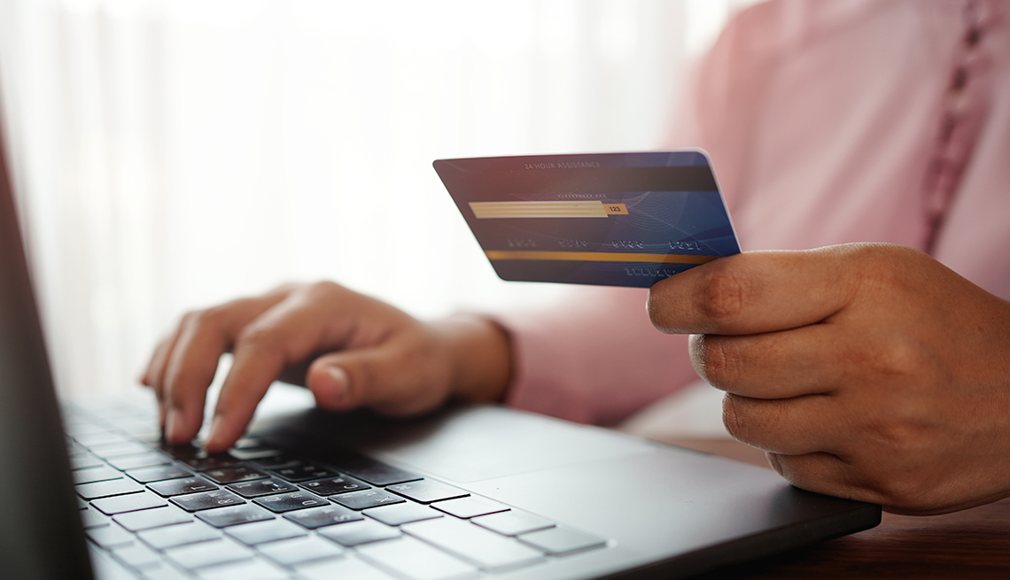mano de una persona sostiene una tarjeta de crédito y con la otra digita su número en una computadora