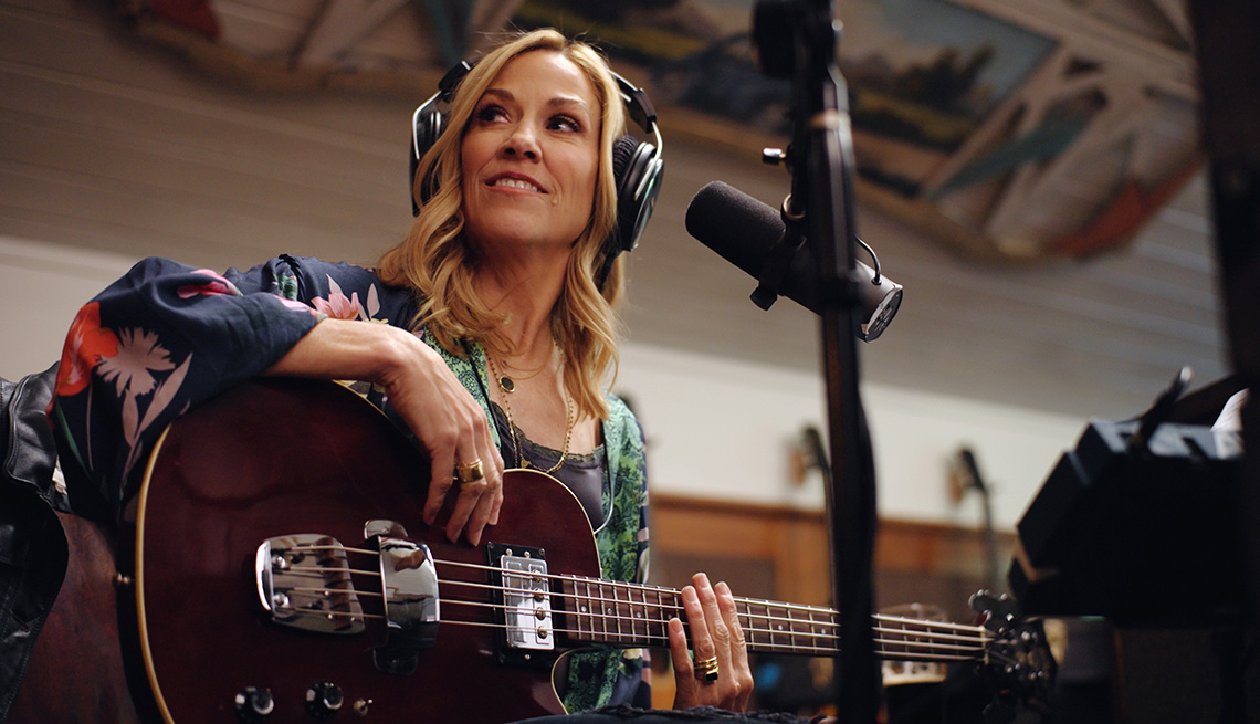 Sheryl Crow con su guitarra usando audífonos y sentada detrás de un micrófono en una escena del documental Sheryl de Showtime