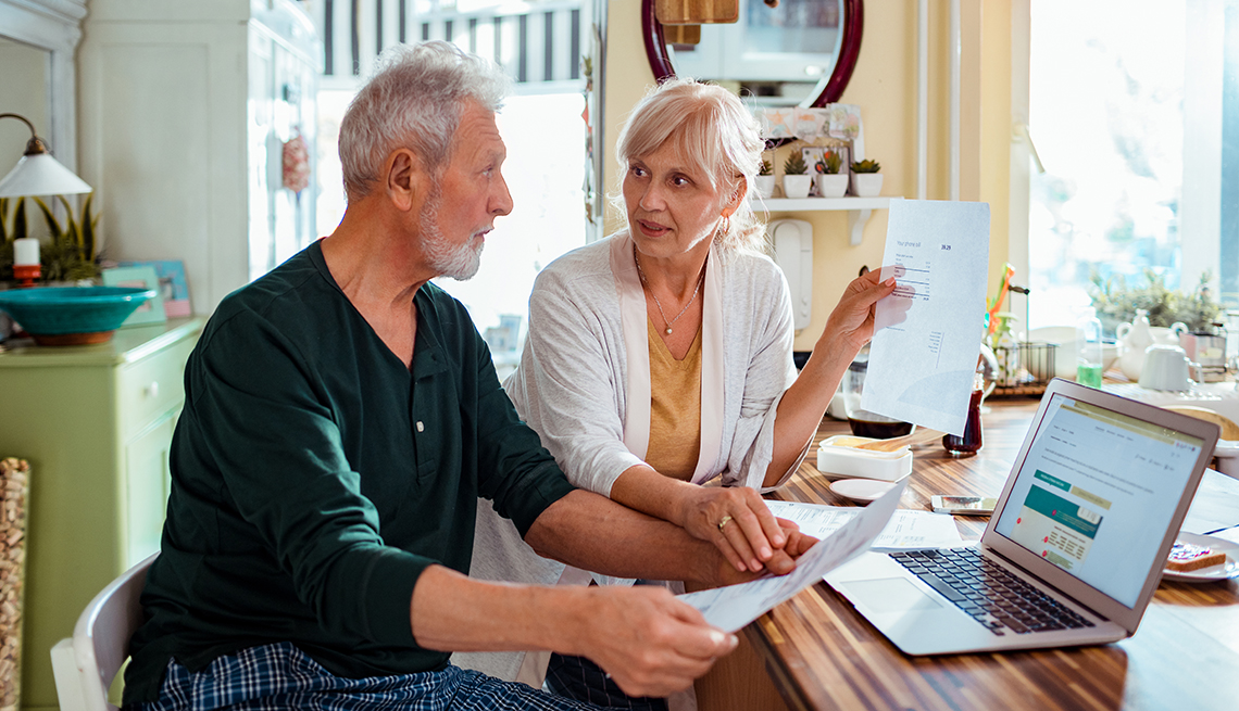 Pareja mayor en la cocina de su casa hace cuentas con una computadora y unas facturas 