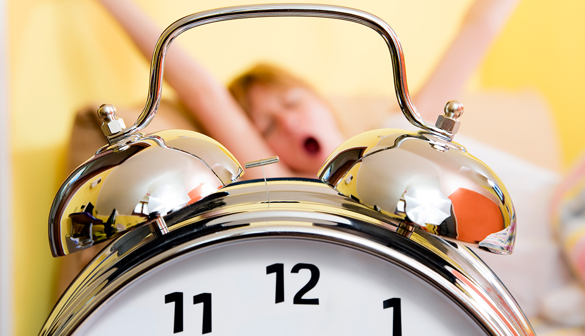 Reloj en primer plano y mujer bostezando al fondo