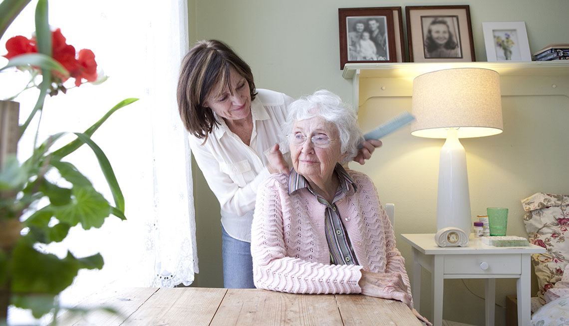 Una mujer le cepilla el cabello a su madre mayor.