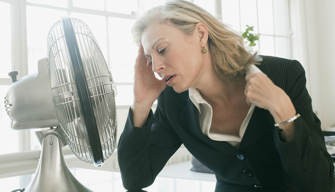 Una mujer con calor sentada frente a un abanico