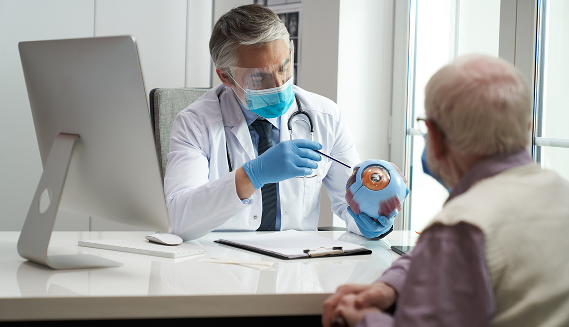 Doctor apunta a un modelo de un ojo mientras un paciente observa Doctor apunta a un modelo de un ojo mientras un paciente observa