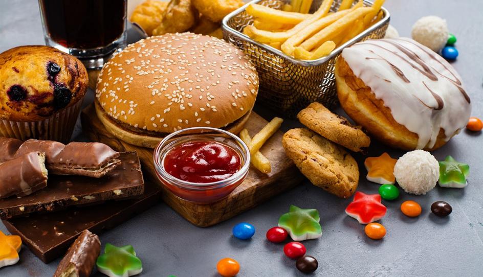Variedad de alimentos procesados entre ellos chocolates, caramelos, una hamburguesa, donas, soda, galletas dulces y papas fritas