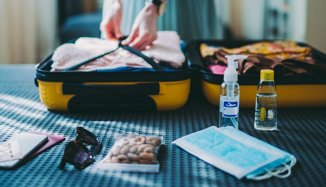 Persona empaca mascarillas y desinfectante para viajar